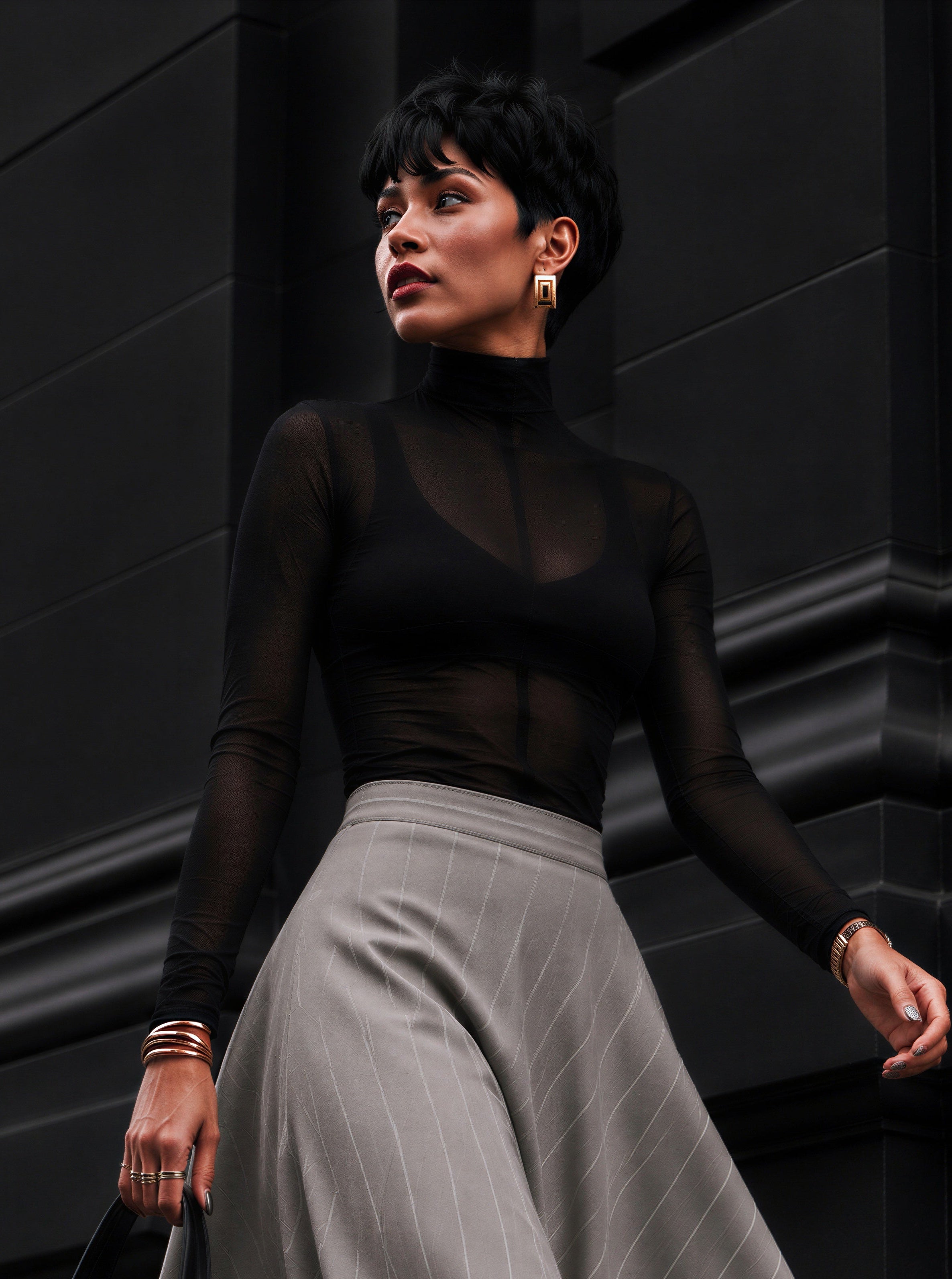 A woman walking outdoors in front of a dark building, wearing a sheer black long-sleeve top, a light gray pinstriped asymmetrical skirt, and black knee-high heeled boots, while carrying a large black handbag.