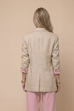 Woman wearing a beige blazer and pink pants against a beige background